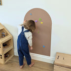 Young child playing with magnetic letters on a clay coloured wall decal