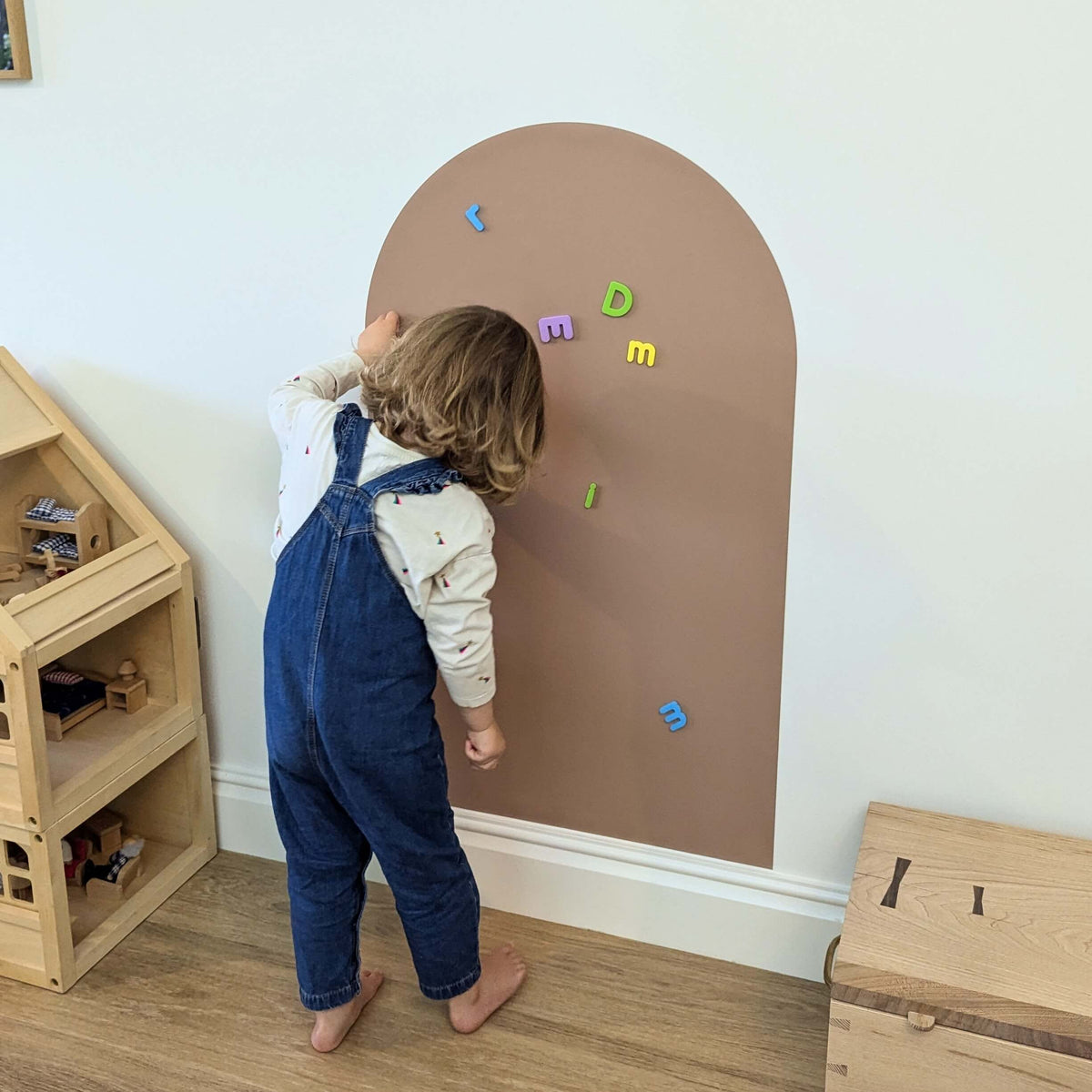 Young child playing with magnetic letters on a clay coloured wall decal